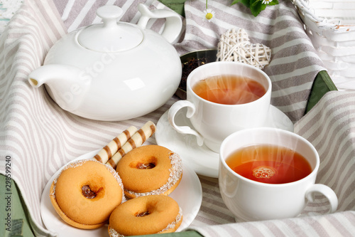 Two cups of hot tea with delicious cookies on white wooden table