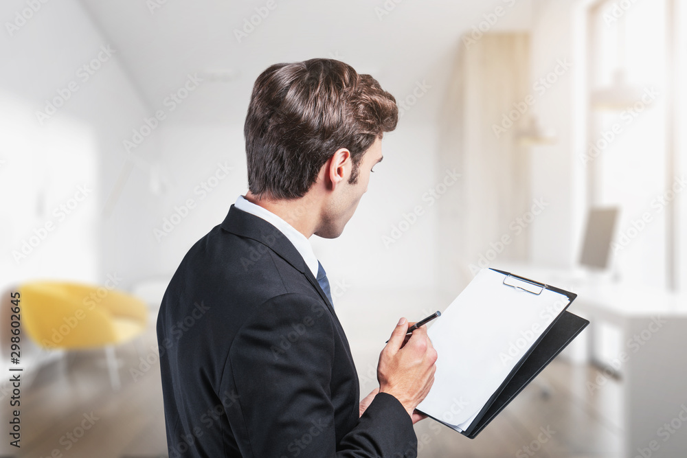 Young businessman with clipboard in blurry office Young businessman with clipboard in blurry office