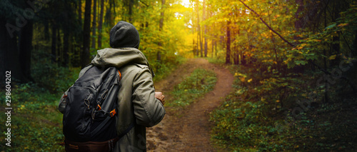 A man with backpack walks in the amazing autumn forest. Hiking alone along autumn forest paths. Travel concept.