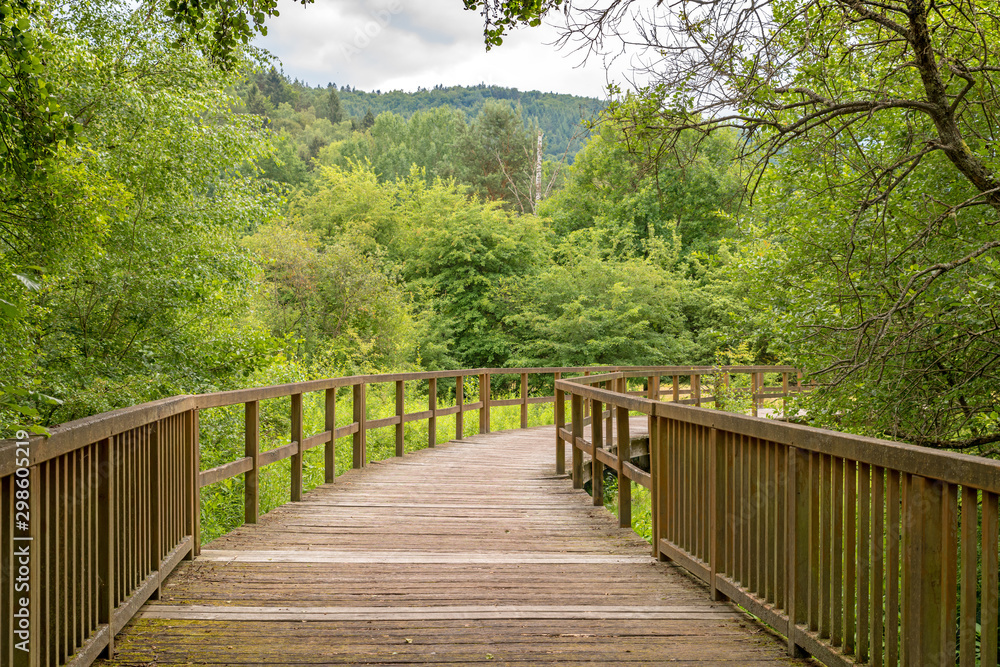 Wooden bridge over a field with meadow and wooded hills