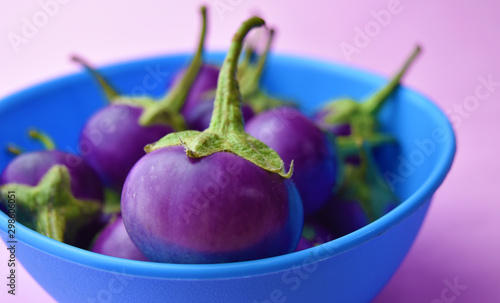 Purple Eggplant fruit in plastic bowl on pink background close up. photo