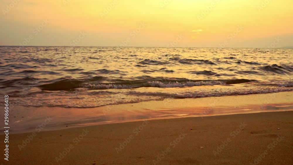 Sunset on the Gulf of Thailand. Orange cloudy sky at sunset. Beautiful sea at orange twilight. Waves slowly wash away traces in the sand.