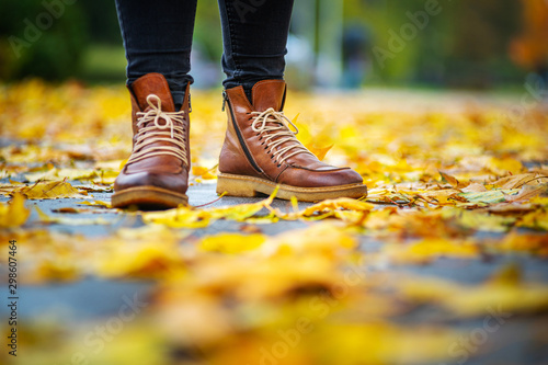 legs of a woman in black pants and brown boots in autumn park on sidewalk strewn with fallen leaves. The concept of turnover seasons. Weather background