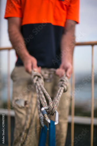 Rope access worker inspector conducting safety inspecting rope rigging tie with safety bunny ears knot prior to used on structure beam roof top high rise building site, Sydney 