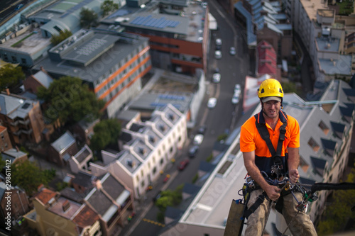 Abseiler maintenance wearing fall safety protection hard hat abseiling fall body harness using hardware device descending from high rise building tools window cleaning gear clipping on harness loop 