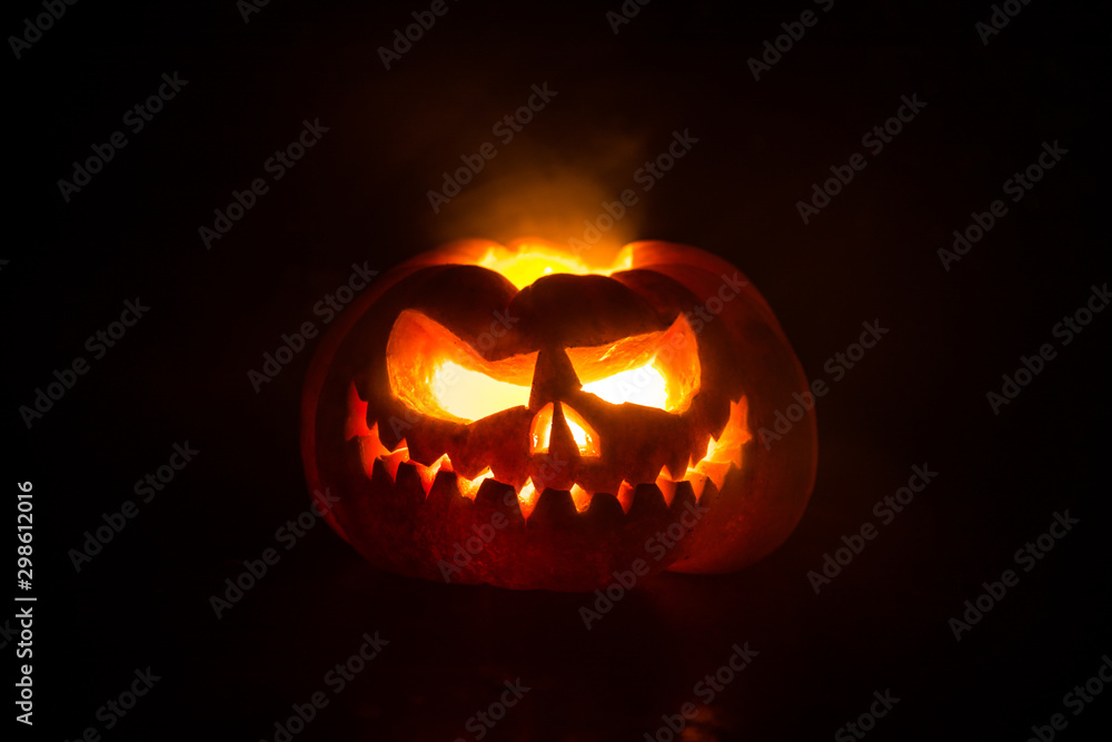 Close up view of scary Halloween pumpkin with eyes glowing inside at black background. Selective focus Close up view of scary Halloween pumpkin with eyes glowing inside at black background. Selective focus