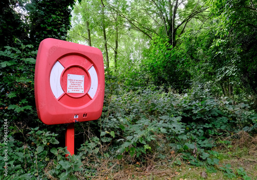 Solitary plastic life ring seen installed in a wooded area by the side of a large lake. Solitary plastic life ring seen installed in a wooded area by the side of a large lake.