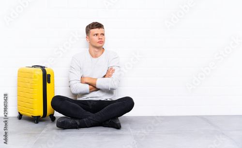 Young handsome man sitting on the floor with a suitcase thinking an idea