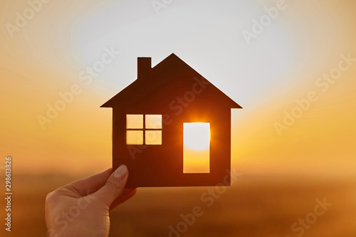 Woman hand holds wooden house against the sun
