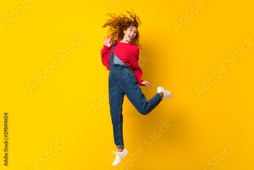 Redhead woman with overalls jumping over isolated yellow wall photo