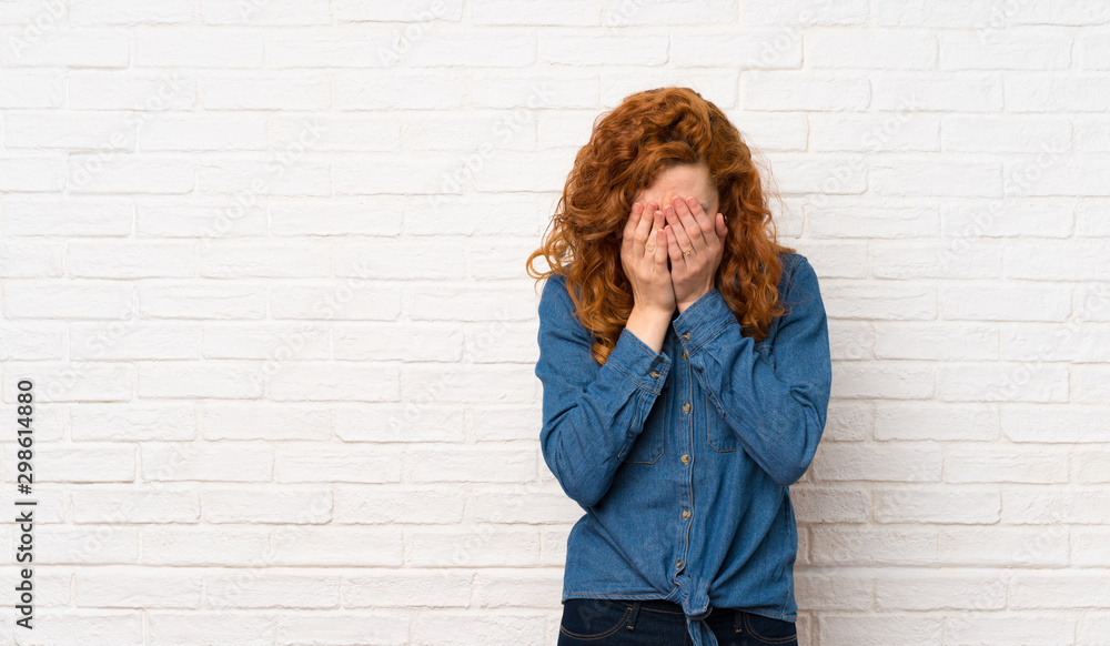 Redhead woman over white brick wall with tired and sick expression