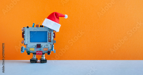 Santa Claus retro monitor computer toy on orange background. Funny Christmas New year greeting card mockup with personal device dressed red Santa hat, blank blue screen, empty backdrop for text