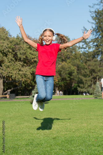 Music of happiness. Happy little child jump high on green grass. Small girl enjoy listening to music in modern headphones. Happiness concept. Feel good. Releasing serotonin dopamine and endorphin