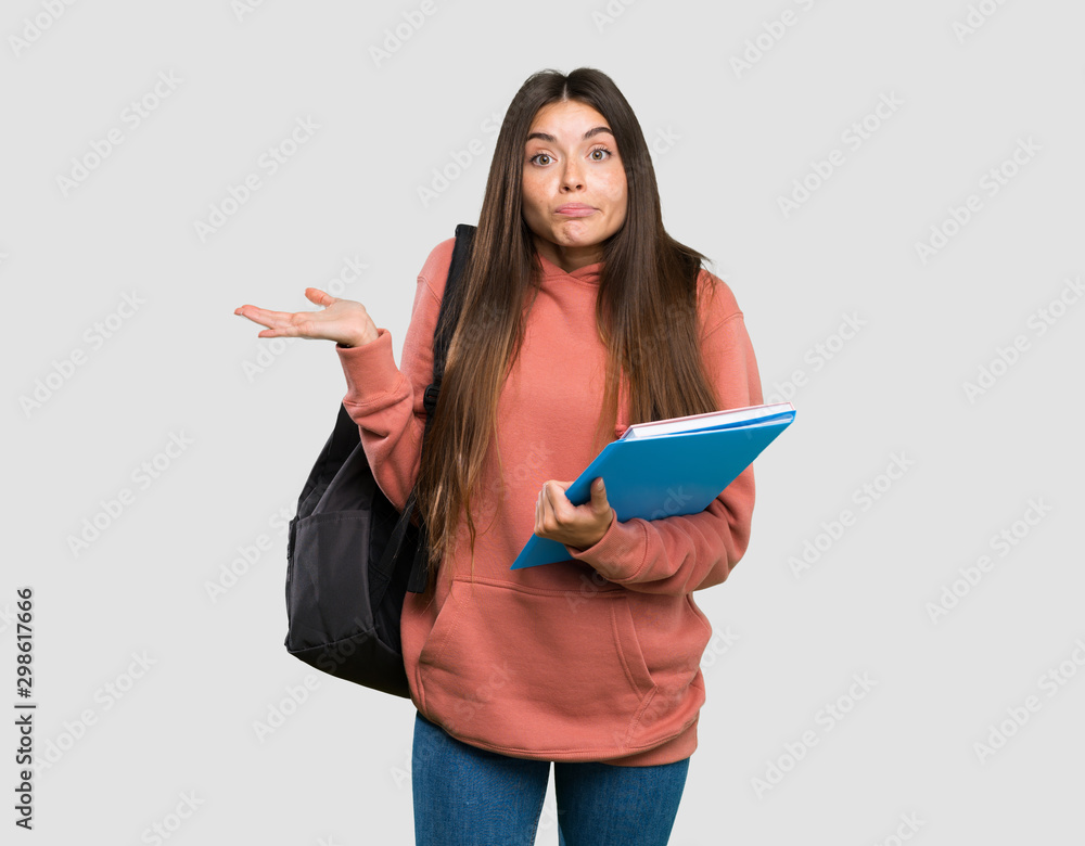 Young student woman holding notebooks having doubts while raising hands over isolated grey background Young student woman holding notebooks having doubts while raising hands over isolated grey background