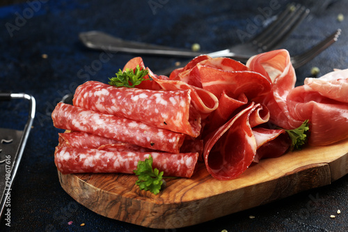 Food tray with delicious salami, coppa, crudo and herbs. Meat platter with selection on rustic table