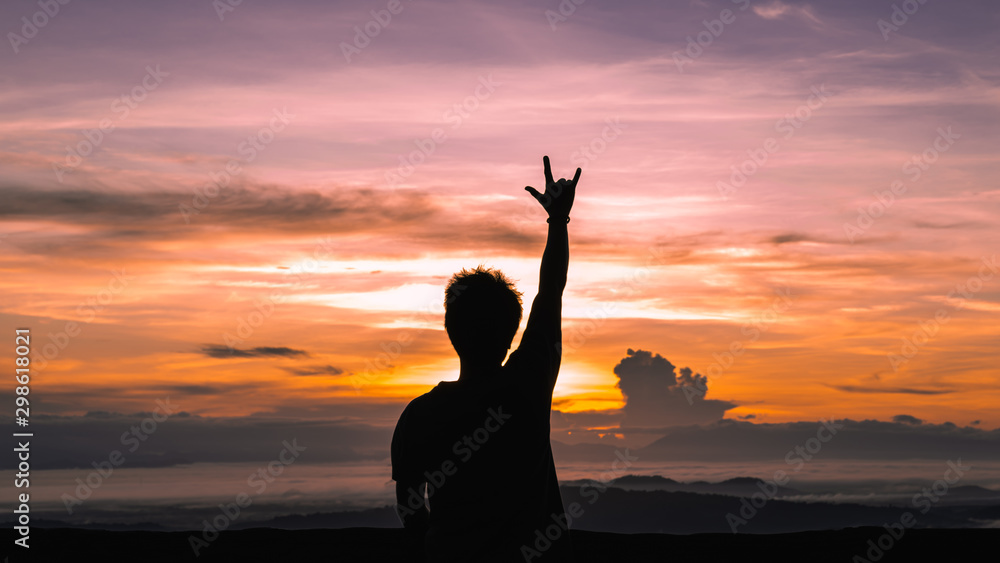 The silhouette of a human being with a raised arm at sunset