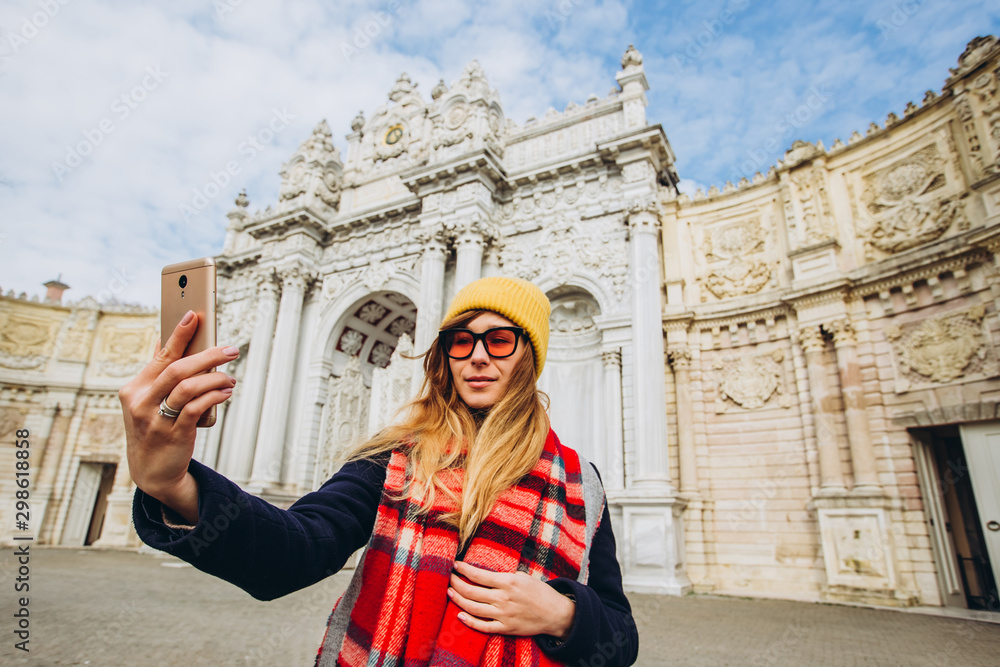 girl takes a selfie in the square in front of Dolmabahce, Istanbul, Turkey. A young girl tourist in a hat and coat is photographed on the phone in front of the Sultan's Palace in Istanbul.