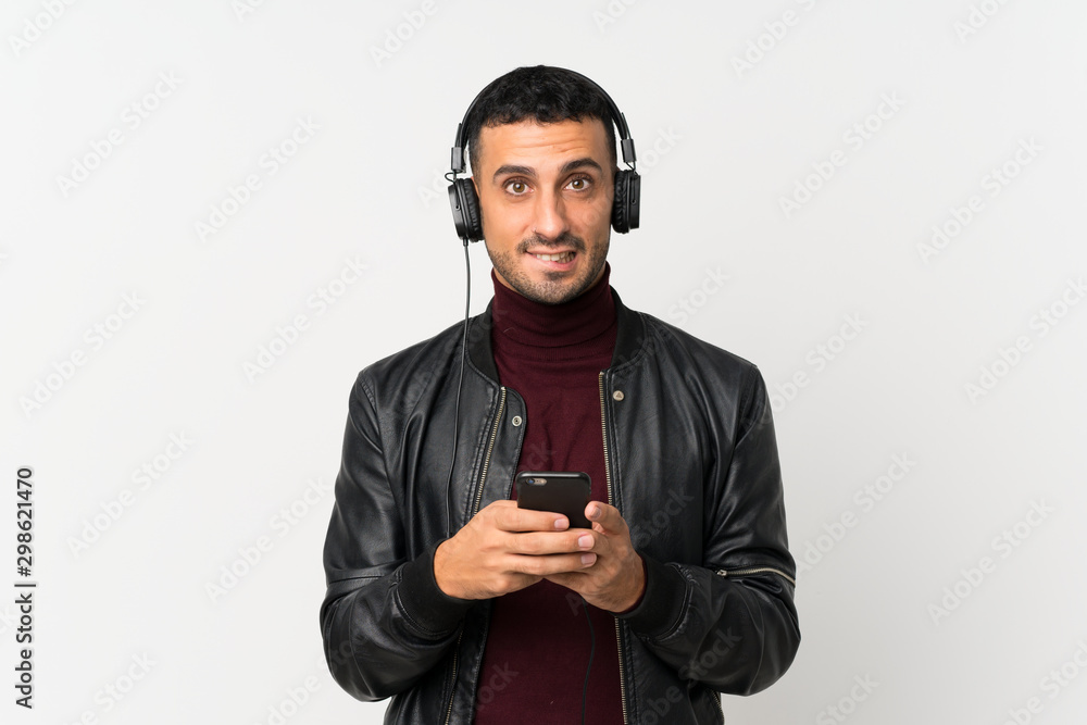 Young man over isolated white background using the mobile with headphones Young man over isolated white background using the mobile with headphones