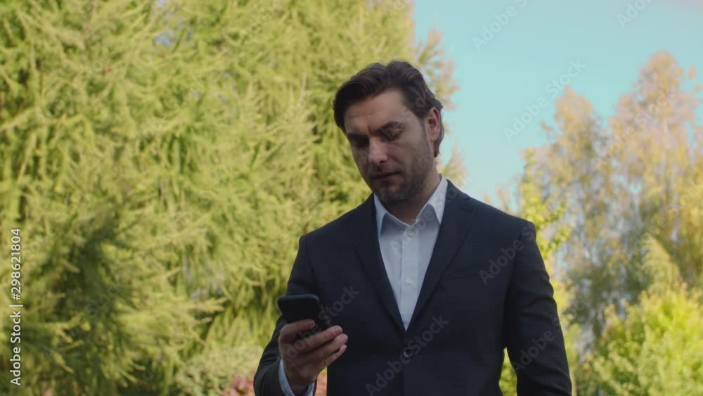 A handsome young guy of European appearance with a slight unshavenness in a business suit is walking in the park. The man laughs and speaks on the phone. A handsome young guy of European appearance with a slight unshavenness in a business suit is walking in the park. The man laughs and speaks on the phone.