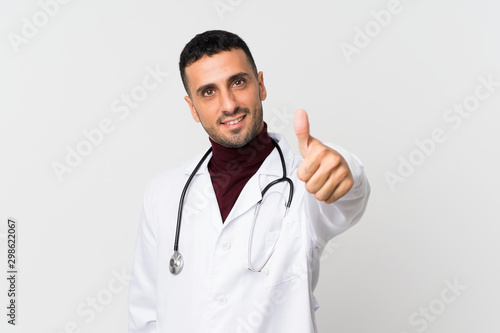 Young man over isolated white background with doctor gown and with thumb up