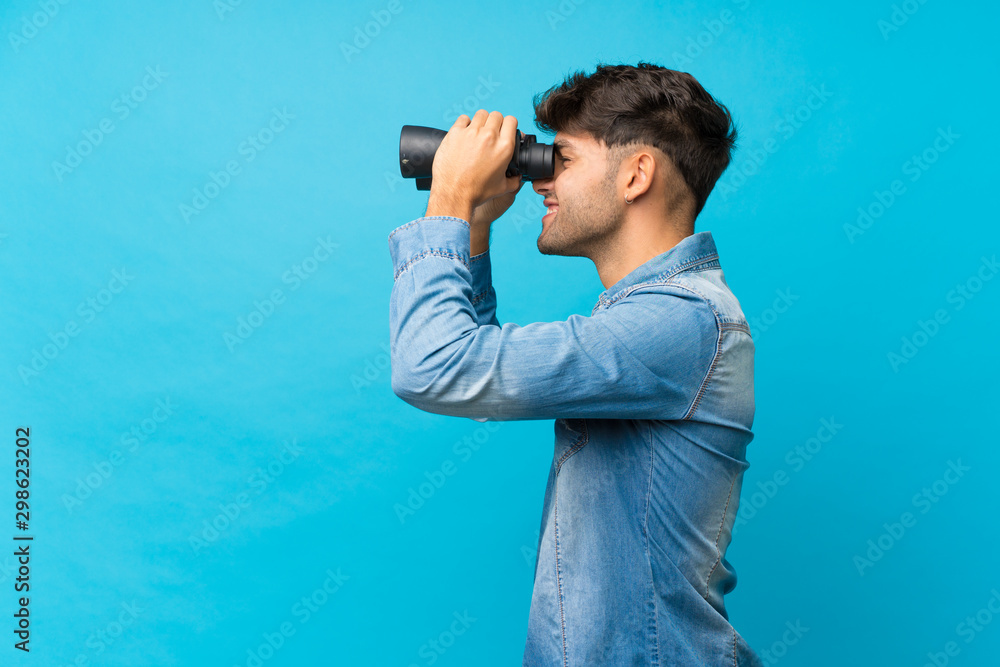 Fototapeta premium Young handsome man over isolated blue background with black binoculars