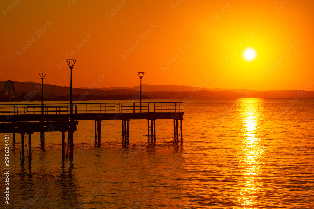 Island of Cyprus. Sunset over the Mediterranean sea. View of the setting sun from the Limassol waterfront. Picturesque wharves on the background of orange sunset. Panorama Of Cyprus.