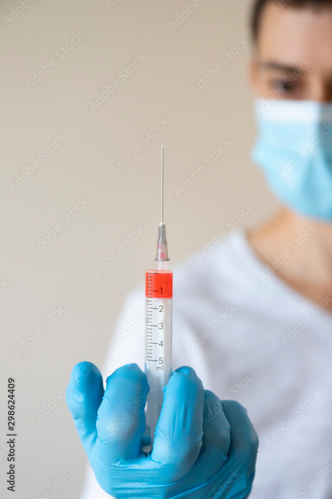 Doctor in mask in blue gloves holding syringe with red liquid Doctor in mask in blue gloves holding syringe with red liquid