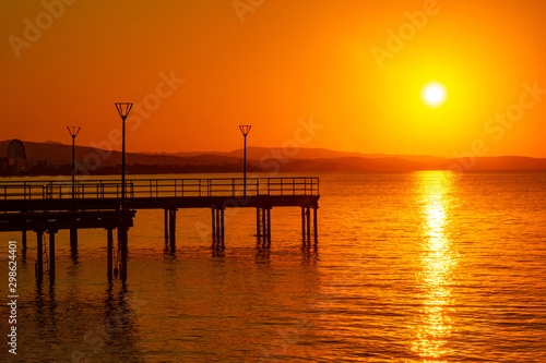 Island of Cyprus. Sunset over the Mediterranean sea. View of the setting sun from the Limassol waterfront. Picturesque wharves on the background of orange sunset. Panorama Of Cyprus.