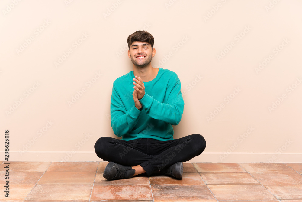 Young handsome man sitting on the floor applauding Young handsome man sitting on the floor applauding