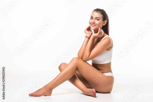 Beautiful woman sitting on the floor with her long shapely legs crossed in front of her wearing her lingerie isolated on white background