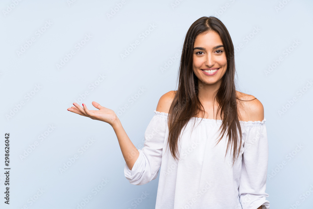 Young woman over isolated blue background holding copyspace imaginary on the palm - obrazy, fototapety, plakaty 