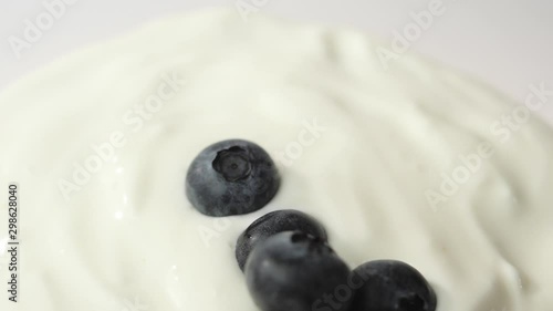 Fresh healthy food. Blueberries falling into yogurt on white background. Fresh fruits splashing in whipped cream. Organic berry, clean eating, dieting, vegetarian, vegan food concept. Slow Motion.