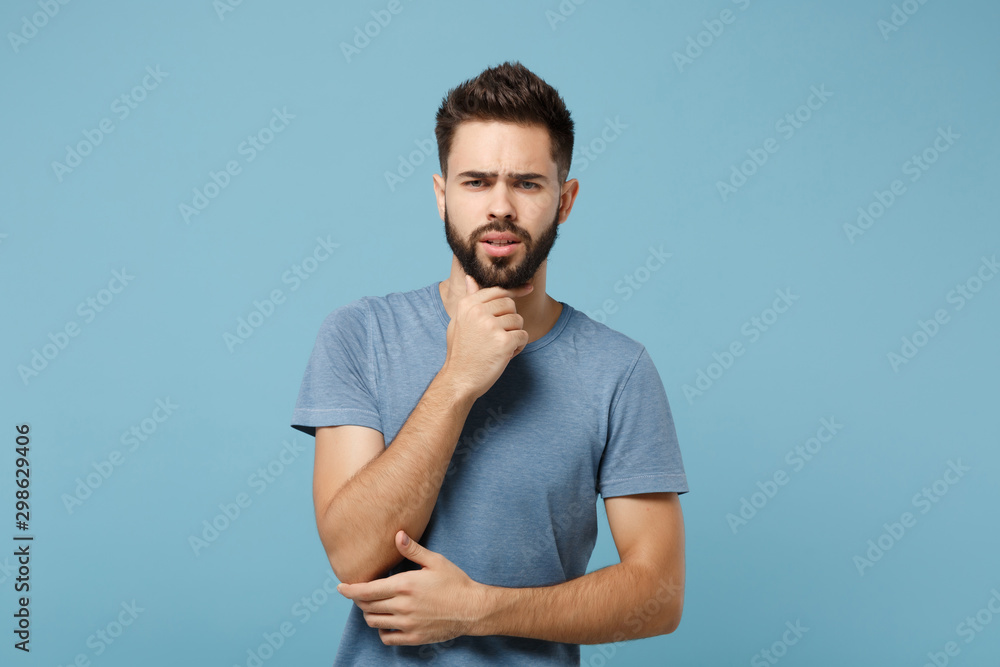 Young preoccupied pensive man in casual clothes posing isolated on blue wall background, studio portrait. People sincere emotions lifestyle concept. Mock up copy space. Put hand prop up on chin. Young preoccupied pensive man in casual clothes posing isolated on blue wall background, studio portrait. People sincere emotions lifestyle concept. Mock up copy space. Put hand prop up on chin.