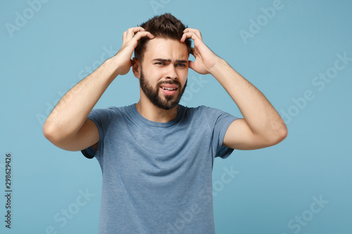 Young nervous preoccupied man in casual clothes posing isolated on blue background studio portrait. People sincere emotions lifestyle concept. Mock up copy space. Looking aside, putting hands on head. © ViDi Studio