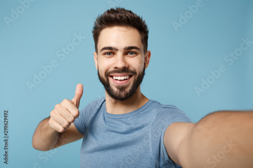 Close up Young handsome man in casual clothes posing isolated on blue background studio portrait. People lifestyle concept. Mock up copy space. Doing selfie shot on mobile phone, showing thumb up. photo