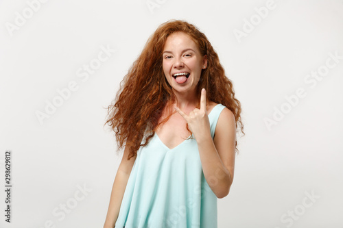 Young pretty redhead woman in casual light clothes posing isolated on white background. People lifestyle concept. Mock up copy space. Depicting heavy metal rock sign, horns up gesture, showing tongue.