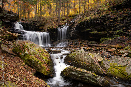 A multi level waterfall surrounded by moss covered rocks and autumn colored trees