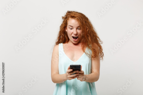 Young shocked redhead woman girl in casual light clothes posing isolated on white background, studio portrait. People lifestyle concept. Mock up copy space. Using mobile phone, typing sms message.