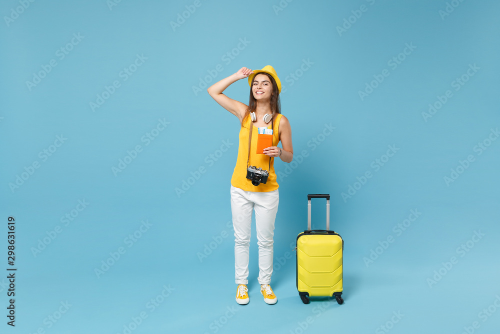 Traveler tourist woman in yellow summer casual clothes hat hold tickets bag camera isolated on blue background. Female passenger traveling abroad travel on weekends getaway. Air flight journey concept Traveler tourist woman in yellow summer casual clothes hat hold tickets bag camera isolated on blue background. Female passenger traveling abroad travel on weekends getaway. Air flight journey concept