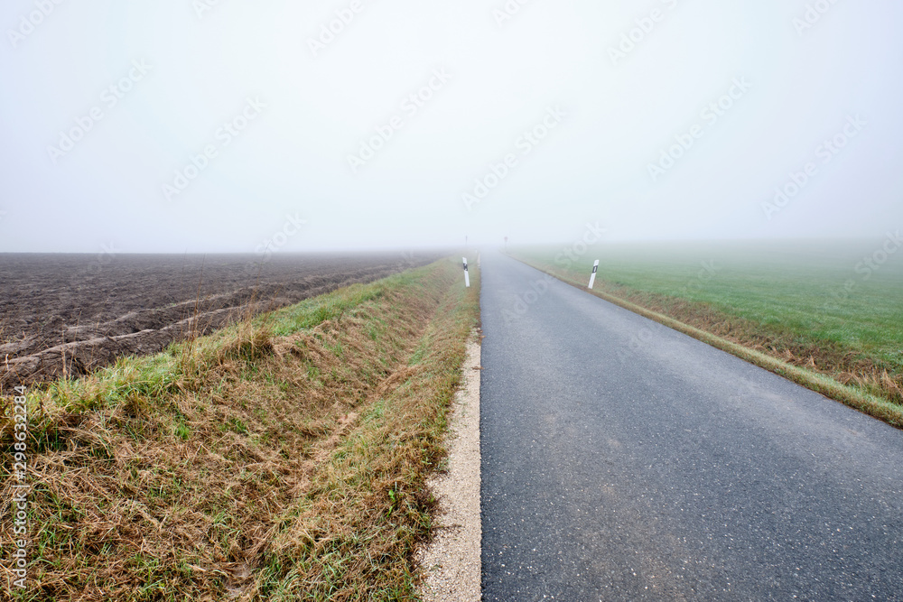 Countryside road to nowhere - narow street with diminishing perspektive leading into the fog. Seen in Germany near Oedenberg, Bavaria in October. Countryside road to nowhere - narow street with diminishing perspektive leading into the fog. Seen in Germany near Oedenberg, Bavaria in October.