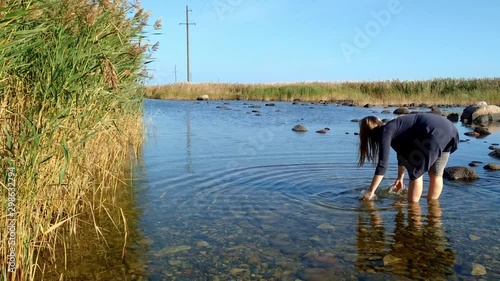 A blonde woman standing in shallow water on Vilsandi Island and cleaning her hands with camera shifting to look at long grass photo