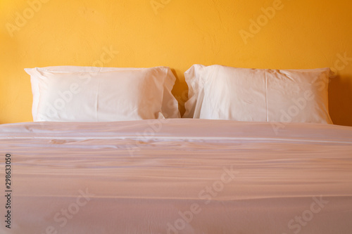 White pillows on cozy bed in bedroom for interior decoration in warming light tone.