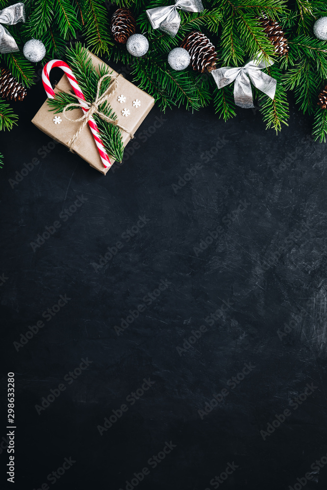 Christmas festive background with christmas tree branches, fir cones and gift box with candy cane on dark concrete stone background.