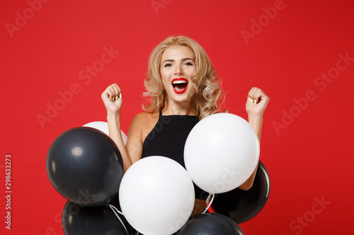 Ovejoyed young woman girl in black clothes posing isolated on red background. New Year 2020 birthday holiday party concept. Mock up copy space. Celebrating holding air balloons doing winner gesture. photo