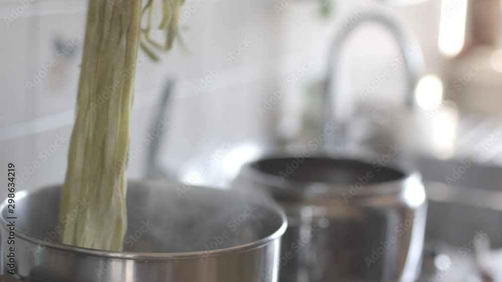 Closeup backlit shot of pouring green vegetable fresh organic pasta fettuccine in a pot with boiling hot water. Shot in 6k, cine lens. Closeup backlit shot of pouring green vegetable fresh organic pasta fettuccine in a pot with boiling hot water. Shot in 6k, cine lens.
