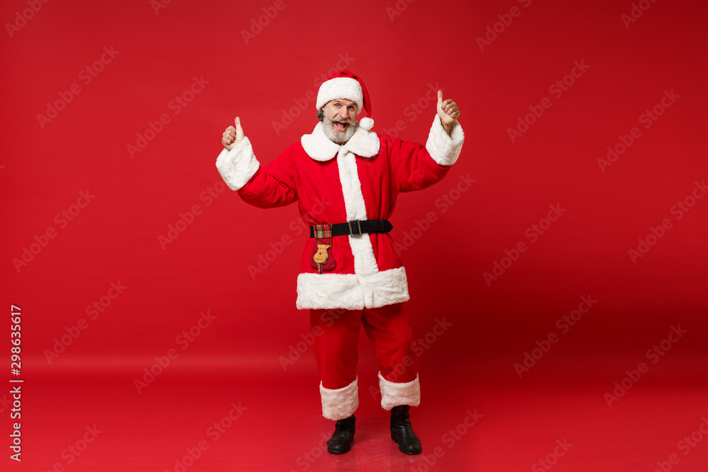 Excited elderly gray-haired mustache bearded Santa man in Christmas hat posing isolated on red wall background. Happy New Year 2020 celebration holiday concept. Mock up copy space. Showing thumbs up. Excited elderly gray-haired mustache bearded Santa man in Christmas hat posing isolated on red wall background. Happy New Year 2020 celebration holiday concept. Mock up copy space. Showing thumbs up.