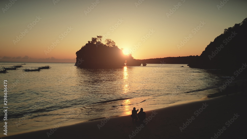 Fototapeta premium Rock Mountain Arch in Sunset Ocean Water. Travel Paradise Tourism Concept. People rest and relax on Beach. Beautiful landscape. Tropical Nusa Penida Bali Island, Indonesia