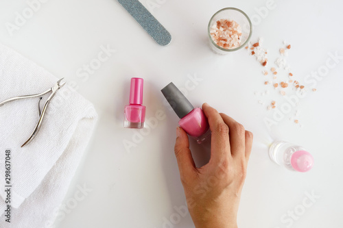 Woman having a manicure iat hpme with the nail tools product on white background, over head view of the hands.