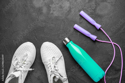 Sports water bottle, shoes and jumping rope on dark background