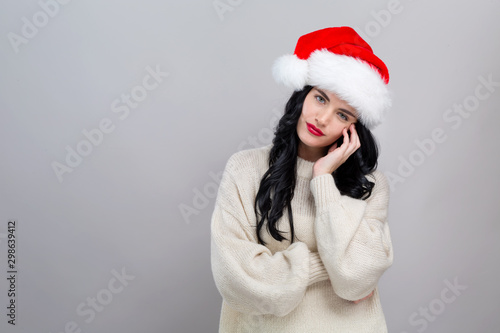 Young woman with Santa hat thoughtful pose on a gray background